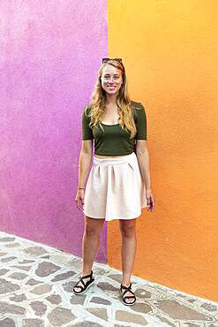 Young woman in dress stands laughing in front of colorful house, orange and pink house facade, Burano Island, Venice, Veneto, Italy, Europe