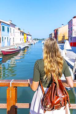 Young woman in front of colorful houses, canal with boats and colorful house facades, Burano Island, Venice, Veneto, Italy, Europe