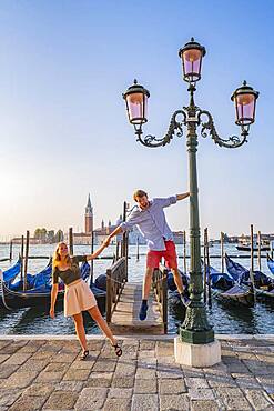 Young happy couple in front of a jetty, Venetian gondolas, in the back church San Giorgio Maggiore, Venice, Veneto, Italy, Europe