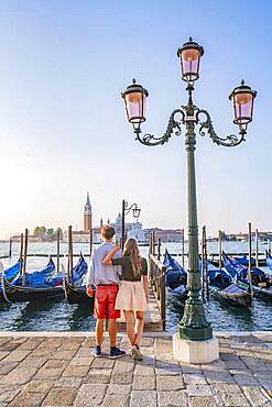 Young couple in front of a jetty, Venetian gondolas, view to church San Giorgio Maggiore, Venice, Veneto, Italy, Europe