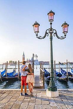 Young couple in front of a jetty, Venetian gondolas, view to church San Giorgio Maggiore, Venice, Veneto, Italy, Europe