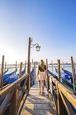 Young woman on a jetty, Venetian gondolas, view of San Giorgio Maggiore church, Venice, Veneto, Italy, Europe