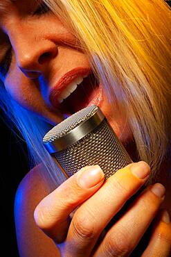 Female vocalist under gelled lighting sings with passion into condenser microphone