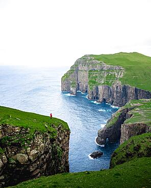 A person standing in the distance in front of Asmundarstakkur cliff, Sandvik, Suduroy, Faroe Islands, Europe