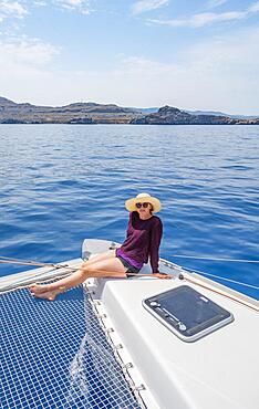 Young woman with hat sitting on deck at the net of a sailing catamaran, sailing trip, Rhodes, Dodecanese, Greece, Europe