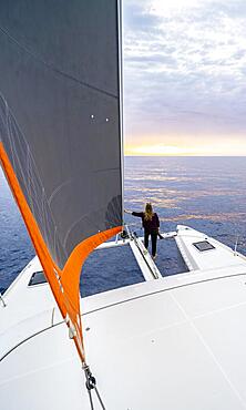 Young woman standing leaning against foresail, catamaran at sunset, Rhodes, Dodecanese, Greece, Europe