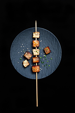 Fried tofu cubes with wooden skewer on plate