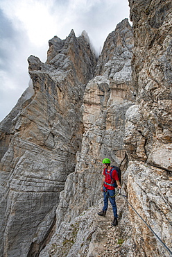 Young man, hiker secured to a steel rope climbing a rock face, Via Ferrata Francesco Berti, Sorapiss circumnavigation, Dolomites, Belluno, Italy, Europe