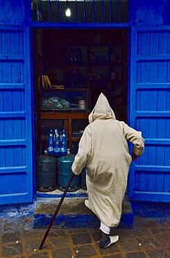 Old man with cane and hooded djellaba walks into shop, old man in beige hooded coat, Blue City, Chefchaouen, Tangier-Tetouan-Al Hoceima, Morocco, Africa