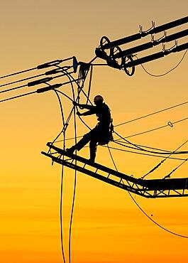 High-voltage fitter at work, backlit by evening sky, overhead power lines, pylons, Baden-Wuerttemberg, Germany, Europe