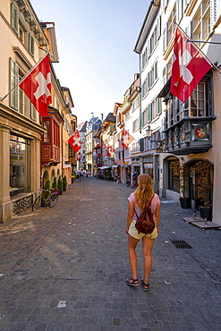 Tourist in Augustinergasse, alleyway with historic houses and Swiss flags in the old town, Zurich, Switzerland, Europe