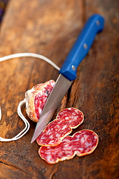 Slicing italian salame pressato pressed over old wood table