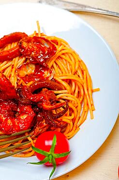 Italian seafood spaghetti pasta on red tomato sauce over white rustic wood table