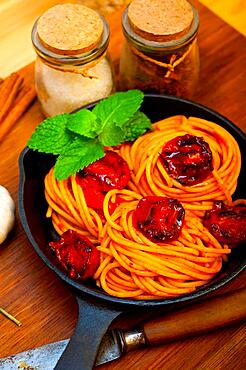 Italian spaghetti pasta and tomato with mint leaves on iron skillet over wood board