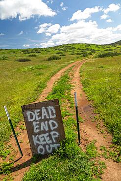 Dead end keep out sign on wire fence at dirt road