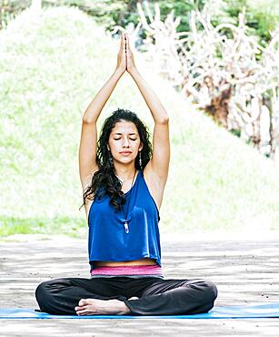 A girl sitting doing meditation yoga outdoors, a woman doing meditation yoga raising her hands up, a young woman doing yoga with her eyes closed