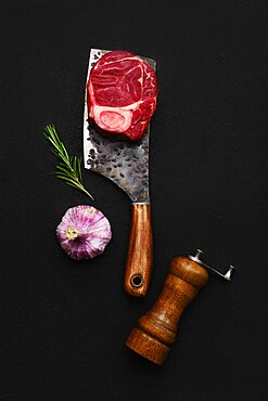 Overhead composition with raw beef ossobuco on butcher cleaver over back background