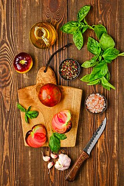 Fresh meaty tomato on wooden cutting board with basil and spice