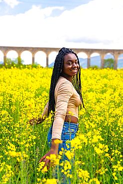 Lifestyle, enjoying nature, portrait of a black ethnic girl with braids, traveler, in a field of yellow flowers