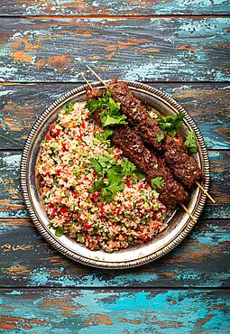 Middle eastern Turkish dinner with meat kebab and couscous salad tabbouleh on rustic metal plate on wooden background top view, traditional Arab meal