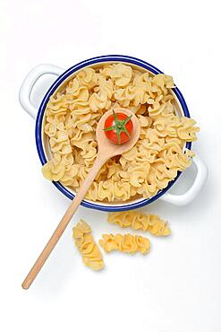 Pasta Capricci, pasta made from durum wheat semolina in bowl and cooking spoon with tomato