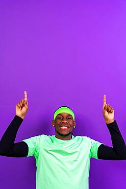 Black ethnic man in green clothes on a purple background, pointing to a free top copy space