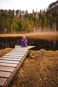 Hiker with backpack sitting on footbridge at lake, Schwansee, Allgaeu, Bavaria, Germany, Europe