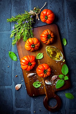 Italian cuisine - Olive oil, tomato and herbs on rustic cutting board