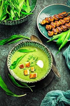 Bear leek soup or ramson soup with crouton, sour cream and turkey skewer on green background