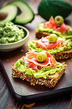 Guacamole dip or spread with open sandwiches and ham on wooden kitchen table