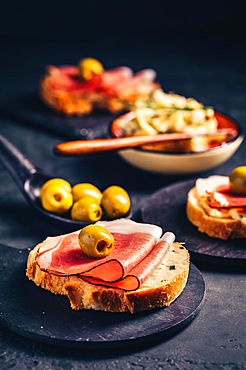 Roasted bread or open sandwich with garlic butter spread and serano ham and olive on dark background