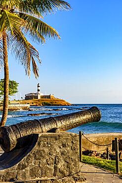 Old cannon from the time of the empire used in the defense of the city of Salvador in Bahia, with Farol da Barra and the sea in the background, Brasil