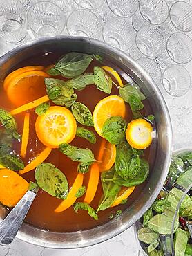 Punch large bowl with oranges and mint. Boiled citrus juice. Drink with a variety of fruits close up. Orange alcoholic cocktail. Empty glasses on the background table. Lifestyle and party concept