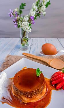 Egg custard with cream and strawberries on a white plate on a blue wooden table with flowers