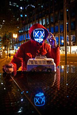 Purge mask, man in red jacket with LED mask. At night, city lights Frankfurt am Main, Hesse, Germany, Europe