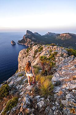 Tourist looking over rocky cliffs and sea, Cap Formentor, coastal landscape, evening mood, Pollenca, Majorca, Balearic Islands, Spain, Europe