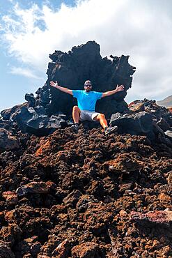 Young tourist sitting on the red stones on the volcanic trail in the village of Tamaduste on the coast of the island of El Hierro, Canary Islands, Spain, Europe