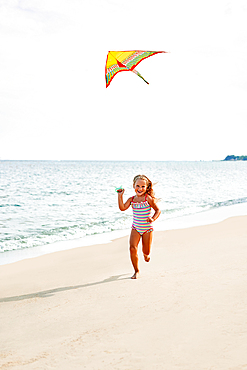 Happy child girl with a kite running on tropical beach. carefree childhood concept