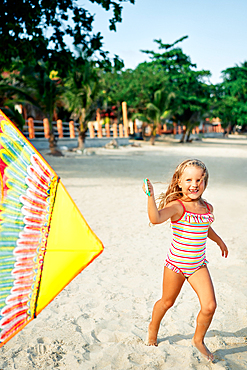 Happy pretty child girl with a kite running on tropical beach in summer. Sea fun, childhood concept