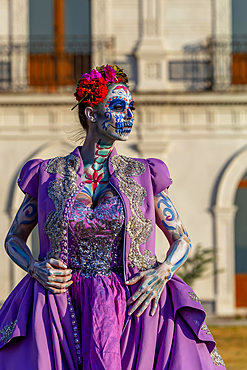 A gorgeous Hispanic Brunette model poses with traditional skull sugar makeup paint for a Mexican festival