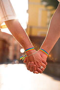 Detail of the holding hands of a couple of homosexual men with the rainbow flag at the pride party in the city, lgbt concept