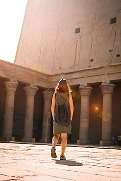 A young tourist wearing a cap visiting the Edfu Temple at sunrise in Aswan. Egypt, with the empty temple in the morning