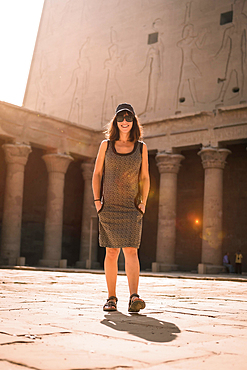 A young tourist wearing a cap visiting the Edfu Temple at sunrise in Aswan. Egypt, with the empty temple in the morning