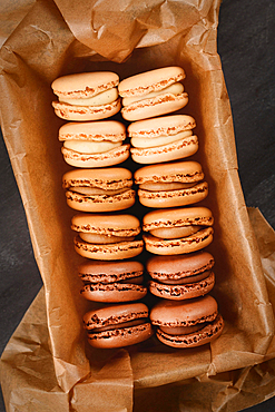 Brown, beige and cream colored French macarons with coffee, mocha, chocolate and vanilla flavor in tray with baking paper