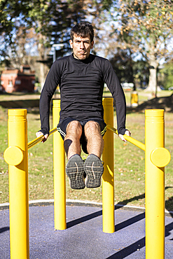 Frotn view of a young man doing abdominal exercises on a public equipment in outdoor fitness