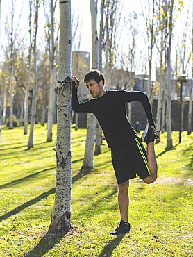 Attractive man leaning against a tree stretching his quadriceps