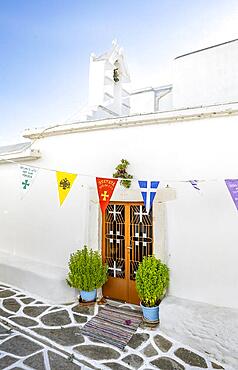 White Greek Orthodox church with colourful flags, picturesque alleys of the village of Marpissa, Paros, Cyclades, Greece, Europe