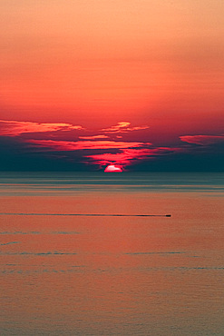 A small boat sails on the sea at a romantic sunset, the sun sinks into the sea at the horizon