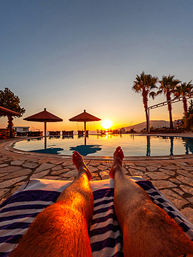 Feet of a man in a pool enjoying a sunset on summer vacation