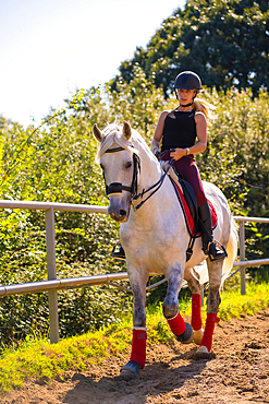 A Caucasian blonde girl riding on a white horse, dressed in black rider with safety hat